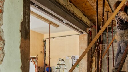 Baufälliger Innenraum eines Hauses. Handwerker steht auf einer Leiter und arbeitet an der Decke.